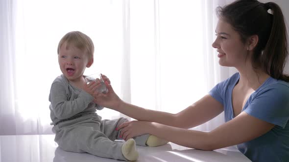 Cute Baby Boy with Tears in Eyes Drinking Pure Water From Glass From Mother Hands and Rejoices in