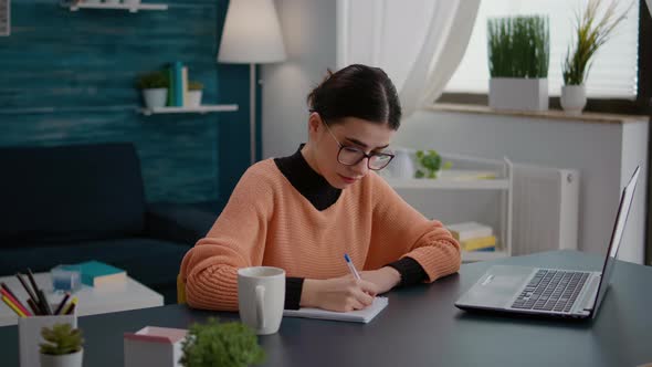 Portrait of Young Student Taking Notes on Textbook in Online Class alt