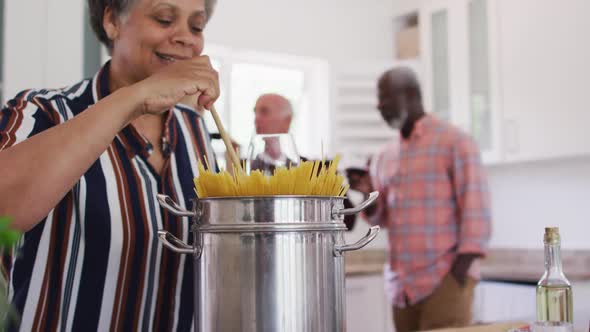 Diverse senior couples drinking wine and preparing pasta in a kitchen