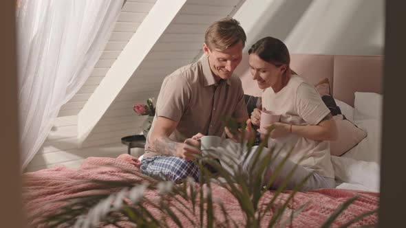 Couple Using Smartphone over Coffee in Bed