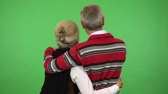 An Elderly Couple Stands with Back To the Camera and Looks at the Green Screen Background in Studio