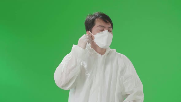 Asian Male Wear Protective Uniform PPE Take Off Glasses, Mask And Smile In Green Screen Studio