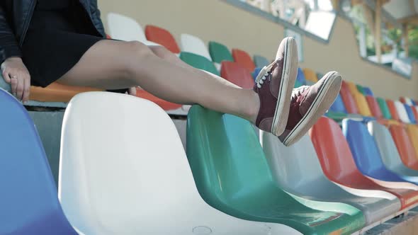 the legs of a woman are hanging on chairs, at the football stadium. feet in red sneakers