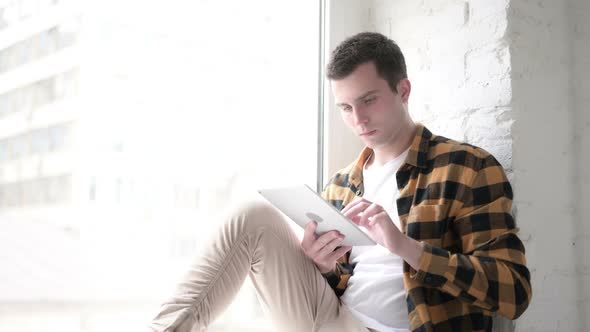 Young Man Using Tablet While Sitting in Window