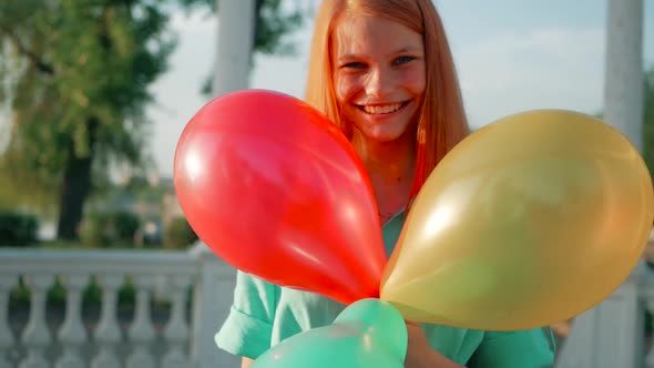 Beauty girl with red hair and colorful air balloons spinning and laughing, on white background. Beau