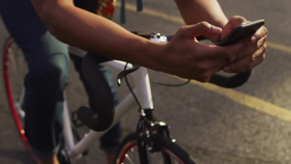 African american man in city, sitting on bike in street using smartphone