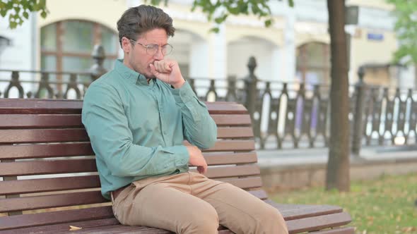 Man Coughing While Sitting on Bench Outdoor