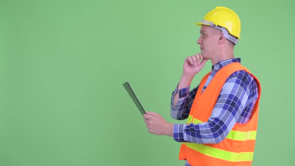 Profile View of Happy Young Man Construction Worker Thinking While Reading on Clipboard