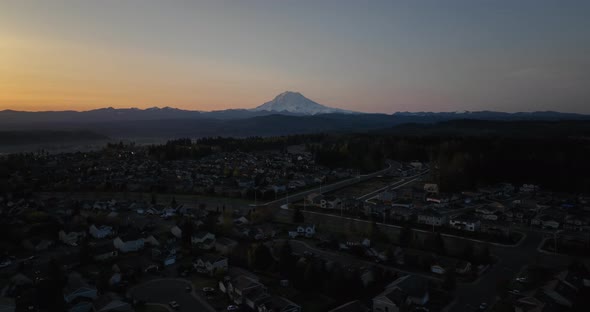 Aerial pushing towards Mount Rainier at sunrise with neighborhoods underneath.