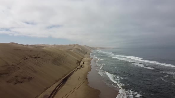 Aerial shot of the stunning dunes on the shore of the ocean, people are walking