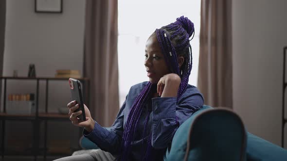 Young Black Woman with Dreadlocks is Resting in Living Room of Her Apartment and Looking on Display