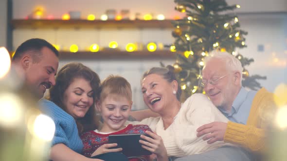 Happy Family Gathered on Couch Together Using Tablet Watching Christmas Photos