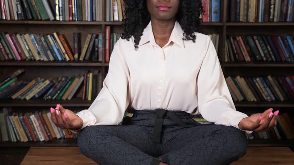 Black Woman in White Blouse Sits in Yoga Pose Lotus on Table