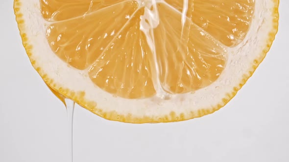 Macro Shot of Flowing the Juice and Oil Stream From Lemon Slice on White Background