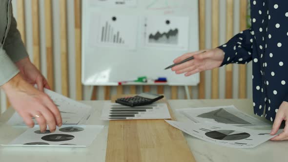 Closeup of Male and Female Hands Pointing at Financial Report with Graphs and Charts