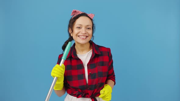 Happy Woman Maid Dancing and Singing Into Mop Like Mic Smiling to Camera Blue Studio Background