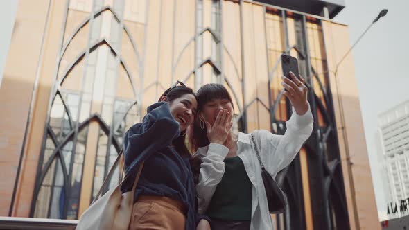 Happy two young women using smartphone video calling her friend while standing on city street.