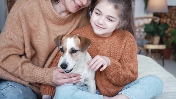 Young Mother Daughter in Knitted Sweaters are Sitting on a Bed in a Cozy Bedroom with Their Small