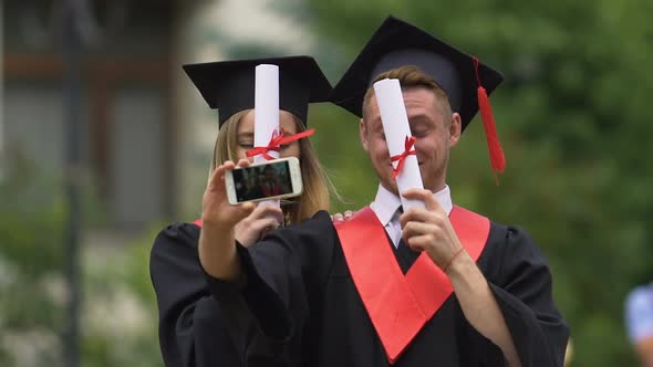 Happy Man and Woman in Academic Caps and Gowns Filming Video on Smartphone