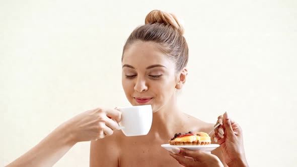 Hands Giving Cake and Cup of Coffee to Young Beautiful Naked Girl in Towel Over White Background