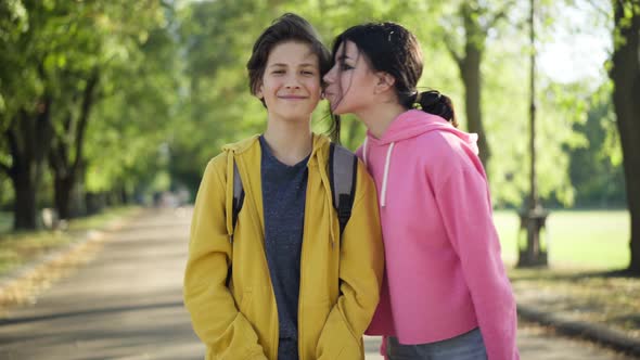 Portrait of Satisfied Teenage Boy Looking at Camera Smiling As Girl Approaching Kissing Cheek Posing