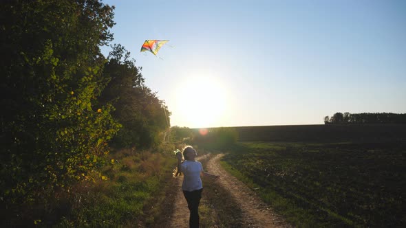 Cute Smiling Girl Jogs with Rainbow Kite on Rural Trail with Sunlight at Background