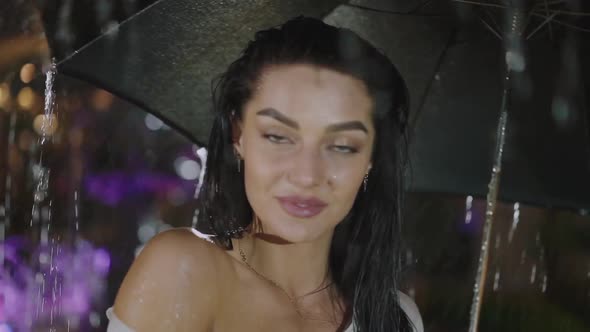 Portrait of Attractive Wet Woman Lightly Flirts at Camera Under the Night Rain