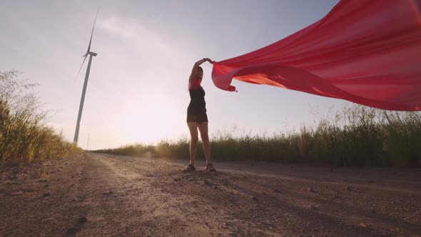 Woman with Pieces of Red Cloth Dance Near the Field with Wind Generators 