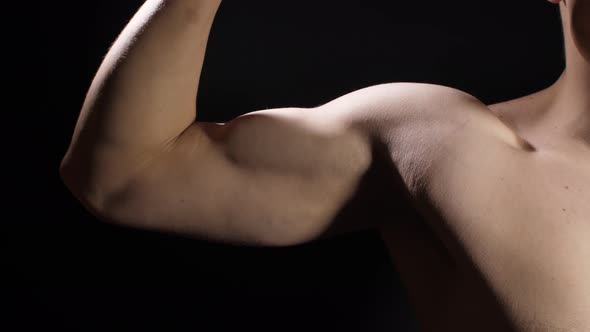 Novice Athlete Demonstrates Biceps on Black Background