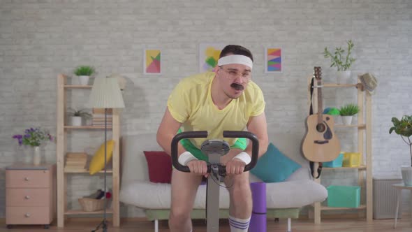 Cheerful Energetic Man Athlete From the 80's with a Mustache Engaged on a Stationary Bike