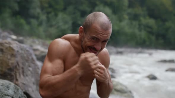 Muscular Man is Training Punches in Nature and Posing for Camera Looking Forward