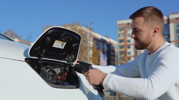 A Male Driver Connects Electric Car to Power System to Charge Car Battery