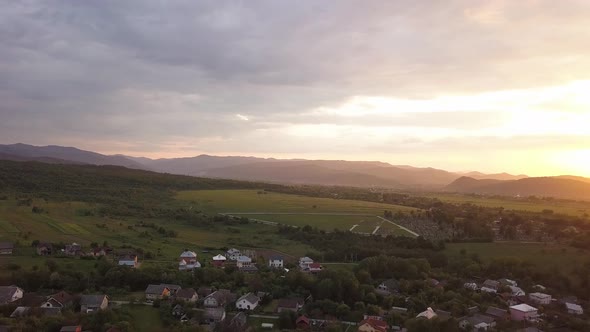 Aerial view of Nadvirna town with scattered houses and distant Carpathian mountain hills at sunset.