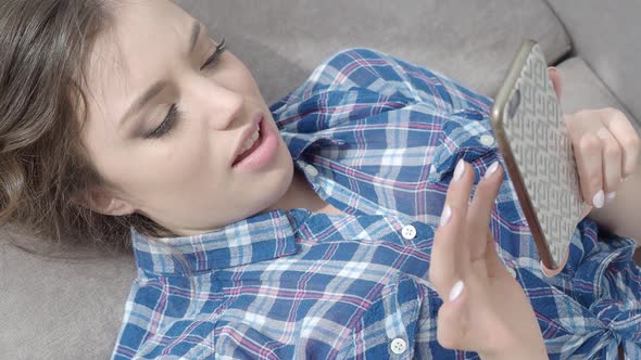 Young Woman is Chatting Online While She is Lying on the Sofa at Home