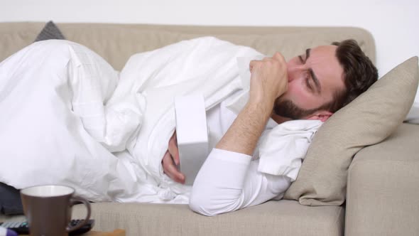 Sick Man Lying on Couch and Blowing Nose