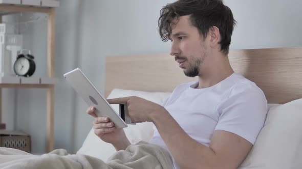 Online Shopping on Tablet By Young Man in Bed