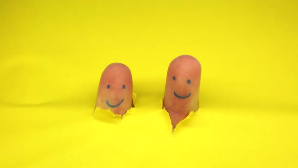 Human Fingers with Smiling Faces Tearing Yellow Paper