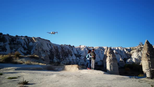 Tourists are Standing on the Edge of the Cliff Among Rocks in Cappadocia and Piloting Drone in a