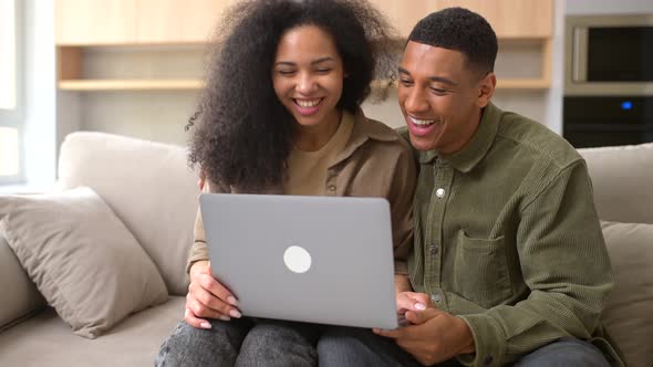 Multiracial Couple Using Laptop for Video Call While Sitting at the Sofa at Cozy Living Room