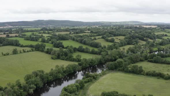 Aerial rises over small river running through lush green pasture land