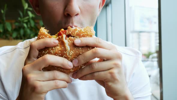 Young Hungry Man Eats Hamburger in a Cafe, Fast Food Restaurant