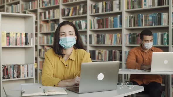 University Students Wearing Face Mask and Sitting with Books and Laptop in Library Social Distance