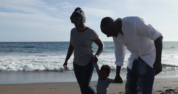 Happy african couple walking on the beach with little son - Black family enjoy vacation together