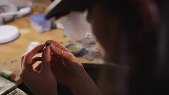 Close up of hands of caucasian female jeweller wearing glasses, checking jewelry at workshop