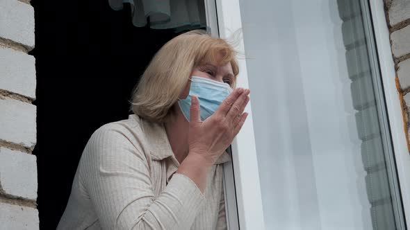 Mature Woman In Medical Mask Wave Goodbye Or Greeting From Window Of House