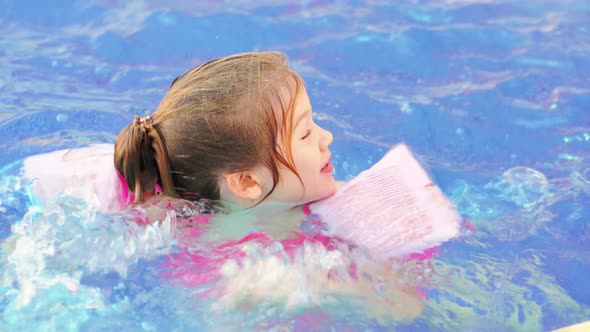 a Funny Little Girl Swims and Plays in Inflatable Armbands in a Pool