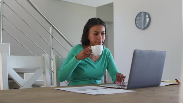 African american woman drinking coffee and using laptop while working from home