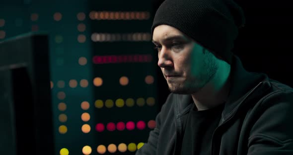 Concentrated Hacker in Sweatshirt and Cap Breaks Into Corporate Servers From His Underground Hideout