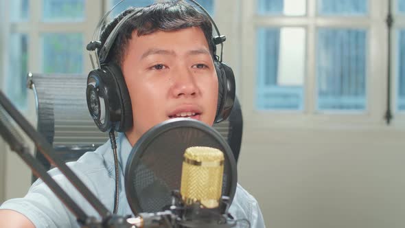 Young Asian Boy In Headphones Playing The Guitar And Singing While Recording Podcast In Studio