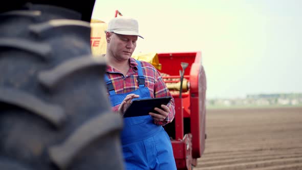 Portrait of Farmer or Agronomist, in Red Plaid Shirt, Is Typing To Tablet Smth, Against Background